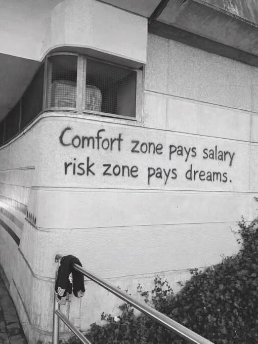 A black-and-white photo of a building corner with spray-painted graffiti reading "Comfort zone pays salary, risk zone pays dreams," paired with a weekend greeting that encourages stepping beyond the comfort zone to pursue one's aspirations.