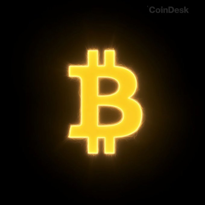 A glowing golden Bitcoin symbol (₿) illuminates against a black background, with the "CoinDesk" watermark in the upper right corner. The luminous crypto icon visually underscores the CoinDesk insight about dormant Bitcoin wallets awakening and moving 553.59 BTC amid record-low dormant Bitcoin movement since Q3 2022.