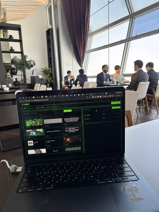 A laptop in the foreground displays a website builder with green-themed content sections, set in a modern lounge where a group of business-attired individuals converse around a table in front of large windows. The scene reflects the post about launching a Robinhood project at the Solana Summit, capturing the blend of development work and networking at the event.