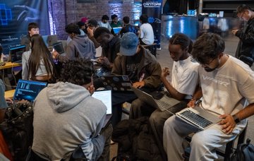 A crowded room of developers sits intently on laptops, deeply engaged in a twelve-hour hands-on Daml hackathon hosted by Canton Foundation, with participants building, problem-solving, and pitching their projects throughout the event.