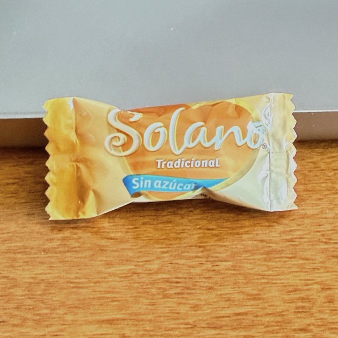 A wrapped "Solano Tradicional Sin azúcar" candy sits on a wooden surface. The product's branding resembles the Solana cryptocurrency, fitting the playful post claiming a new "@solana" product.