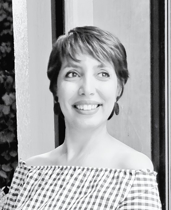 A black-and-white portrait captures a smiling woman with short hair wearing a checkered off-the-shoulder top, her youthful appearance highlighting the caption's claim of being 42 years old.