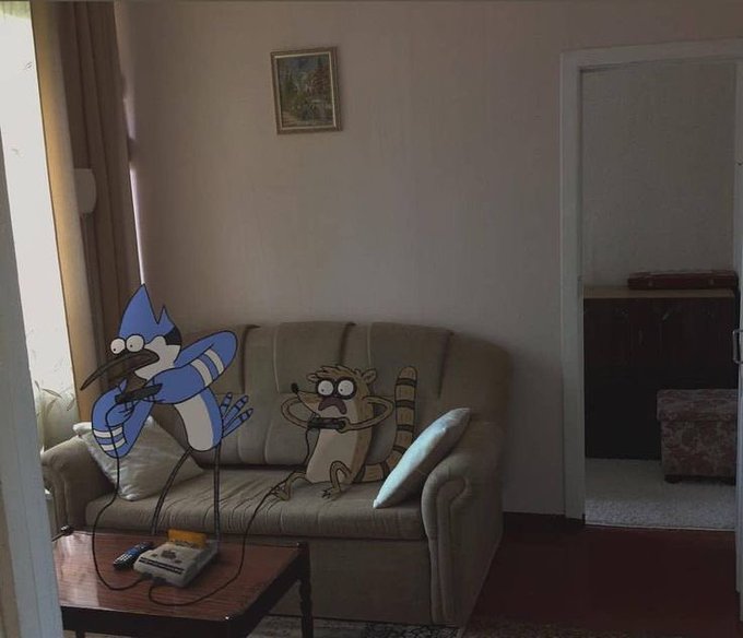 A real living room featuring a couch with animated Mordecai and Rigby from Regular Show superimposed, playing a retro video game console on the floor.