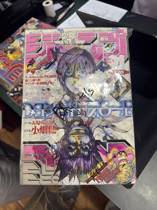 A copy of Weekly Shōnen Jump featuring Death Note by Takeshi Obata and Tsugumi Ohba (Issue No. 14, ¥220) rests on a table, the iconic cover art autographed in black marker. The autographed manga exemplifies the rare collectibles and grails featured in the @phygitals repack drops highlighted in the post.