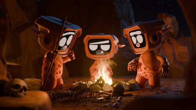 Three cartoonish robot figures in prehistoric clothing gather around a campfire in a dark cave, with a skull visible on the ground.