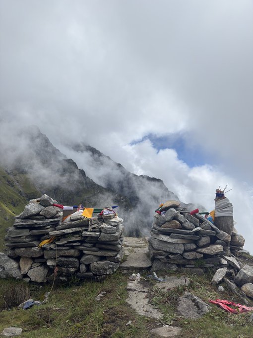 Two stone cairns adorned with colorful prayer flags sit on a misty mountain landscape under cloudy skies.