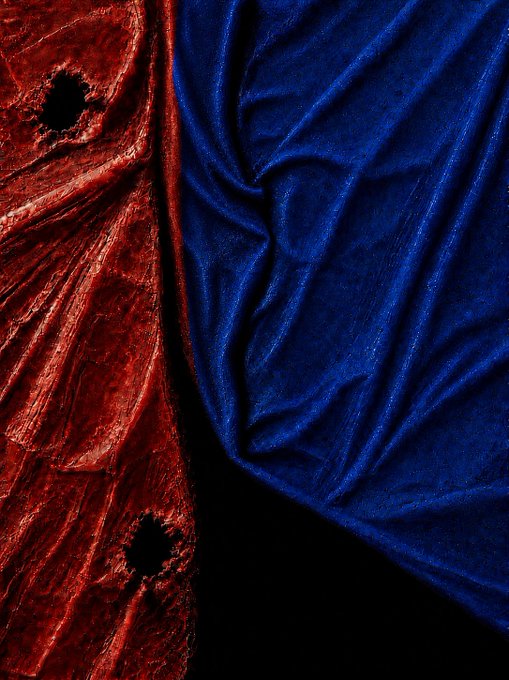 A close-up of luxurious fabric textures, showing deep red velvet with subtle patterned holes on the left and royal blue velvet with rich folds on the right against a dark background.