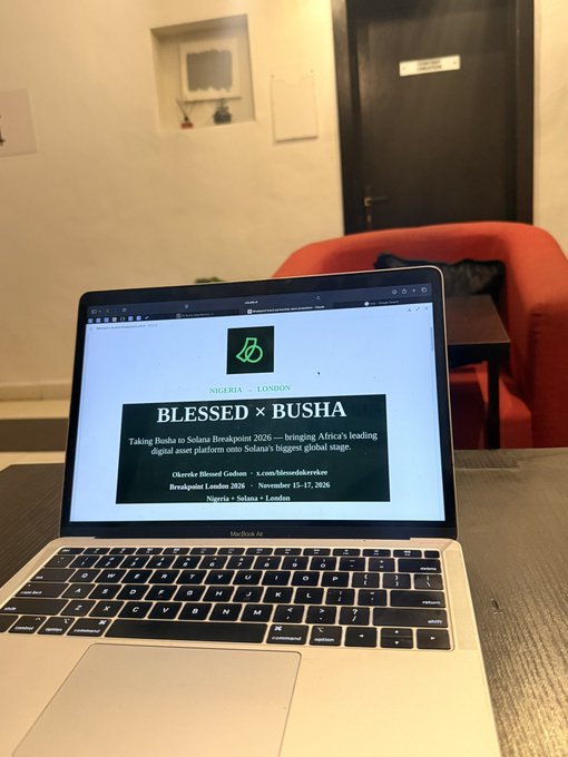 A MacBook Pro on a table displays a website announcing 'BLESSED x BUSHA' as Busha takes over Solana Breakpoint 2026, listing Olerekeke Blessed Godson as a brand ambassador.