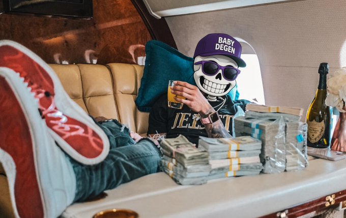 A stylized photo featuring a skull-faced figure wearing a 'BABY DEGEN' cap and sunglasses, reclining inside a luxurious vehicle with stacks of cash, a bottle of wine, and another person's red sneakers visible.