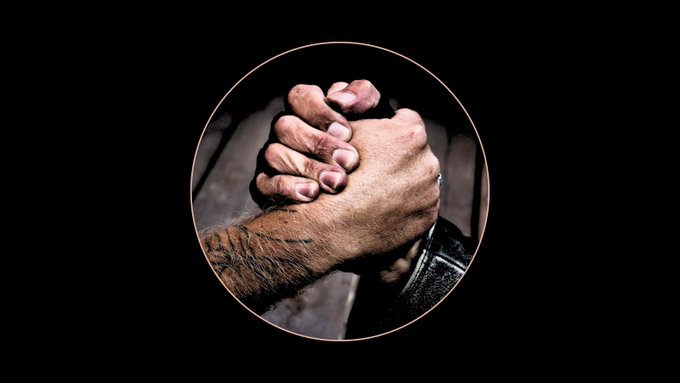 A circular framed image showing a close-up of two hands clasped together, one wearing handcuffs, set against a black background.