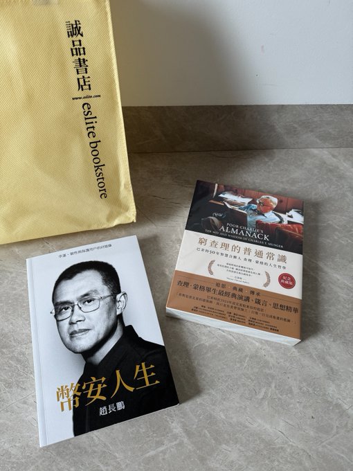 Two Chinese books—one titled '酷安人生' by 赵长鹏 (CZ) and the 'Poor Man's Almanack'—rest next to a yellow 'eslite bookstore' (誠品書店) paper bag on a tiled floor.