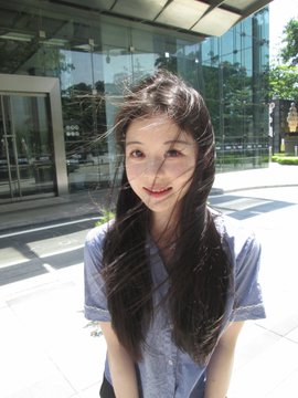 A young woman with long dark hair smiles at the camera while standing outside a modern glass building, her hair tousled by the breeze. The image's bright, sunlit corporate setting complements the post's announcement of her transition to a new role at a US dollar fund in Silicon Valley.