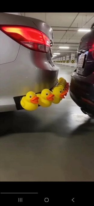 A humorous photo in an underground parking garage showing a car with an unusual decorative trailer attached featuring a row of rubber ducks chained together.
