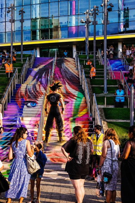 A vibrant outdoor staircase painted with an anime-style mural featuring a character with spiky hair and Japanese kanji, with people gathered around the base and sides.