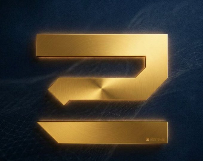 A metallic gold, beveled emblem resembling a stylized angular '2' or 'Z' sits on a dark textured background, with a tiny engraved mark near the lower right.