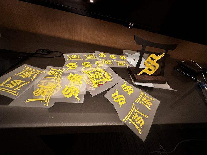A collection of yellow and gold stickers and decals featuring various dollar sign ($) designs are scattered on a table next to a wooden stand.