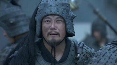 A close-up of a man with a goatee wearing ornate, studded ancient Chinese military armor, with other soldiers blurred in the background.