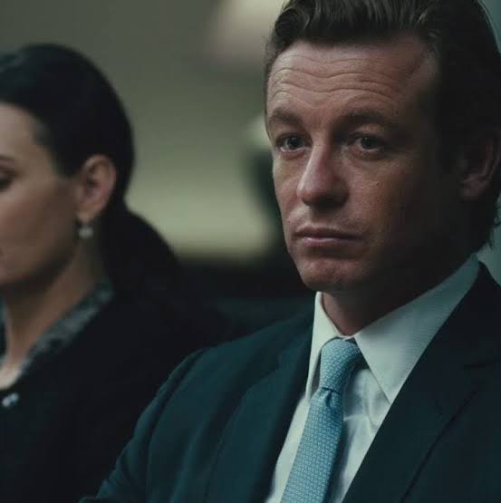 A man in a navy blue suit with a light blue tie and white shirt gazes intently, his serious, contemplative expression embodying the high-stakes tension of trading, as the caption warns about the perils of mistimed market execution. Behind him, a partially visible woman with dark hair reinforces the pressure-filled atmosphere of a financial decision-making moment.