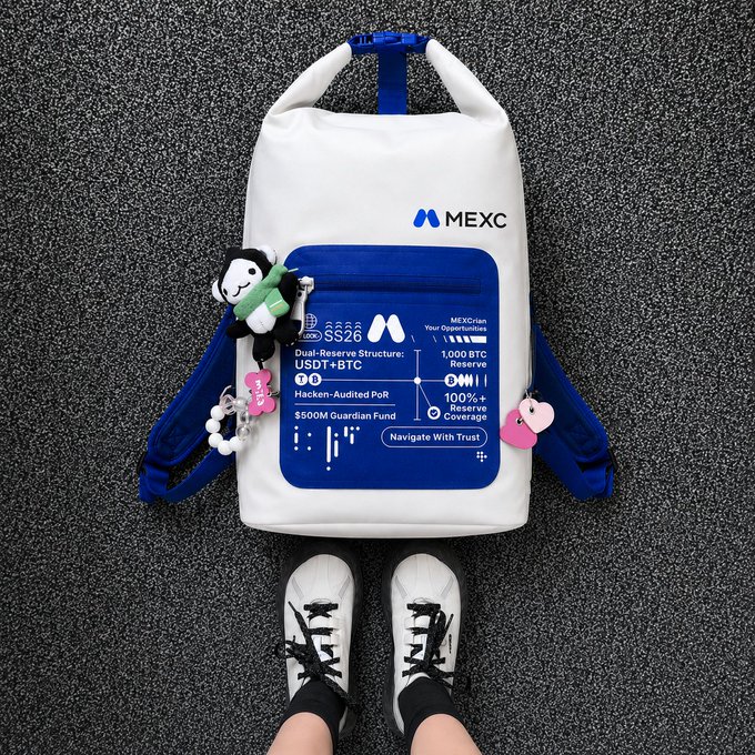 A white MEXC-branded backpack with blue straps, decorated with plush keychains and labeled with details like "USDT+BTC," "1,000 BTC Reserve," "100% Merkle Coverage," and "Navigate With Trust," sits on asphalt next to a pair of white sneakers—capturing the relaxed spirit of a crypto-friendly weekend getaway where trading essentials travel alongside everyday gear.