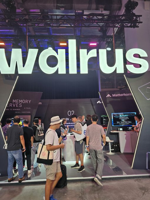 A busy exhibition booth with a large illuminated 'walrus' sign, featuring sub-displays for 'MEMORY CURVES' and 'Matterhorn' as attendees interact with staff and screens.