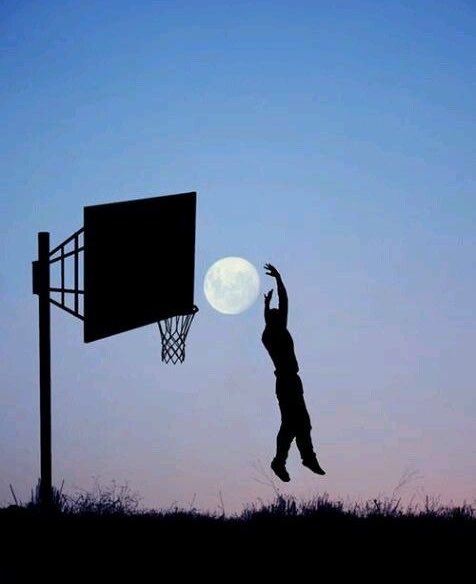 A silhouette photograph of a basketball player jumping toward a hoop with the full moon perfectly aligned behind the basketball.