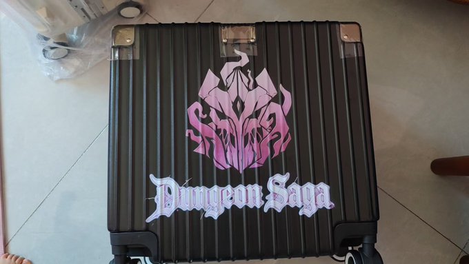A black ribbed suitcase with a pink dragon emblem and the text "Dungeon Saya" in stylized white lettering, sitting on a tiled floor.