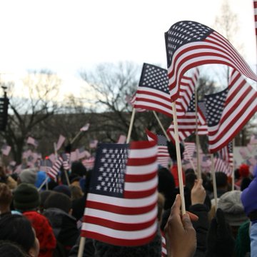 A crowd waves small American flags at a public gathering, their red, white, and blue colors standing out against the winter sky. The patriotic scene of engaged citizens visually echoes the survey's finding that Americans show strong interest in forward-looking financial innovations while remaining anchored to traditional values.