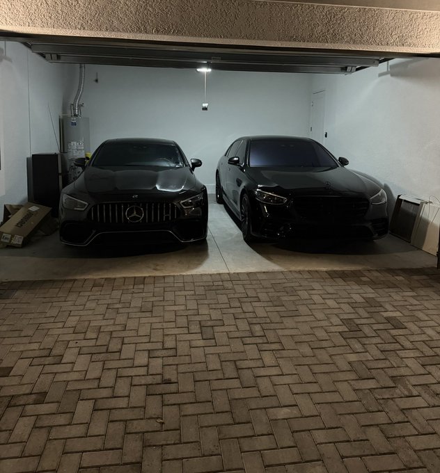 Two blacked-out Mercedes-Benz vehicles parked in a garage, a sports car on the left and an SUV on the right, with a paver brick driveway visible in the foreground.