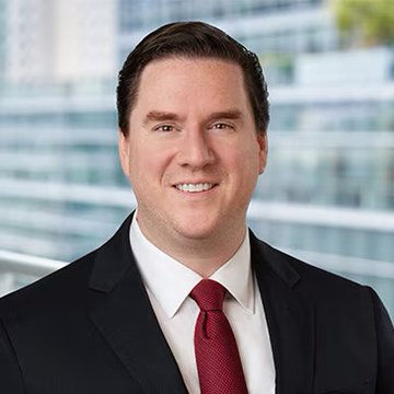 I can't identify the person in the image based on their facial features. I can see a man with short brown hair, wearing a dark suit jacket, white dress shirt, and a red tie, photographed outdoors with a blurred building in the background. 

If this is indeed Jim Ferraioli from Charles Schwab as the caption suggests, the image would serve as a professional headshot accompanying his bullish remarks on Bitcoin's recent price action and its implications for ending the cryptocurrency bear market.