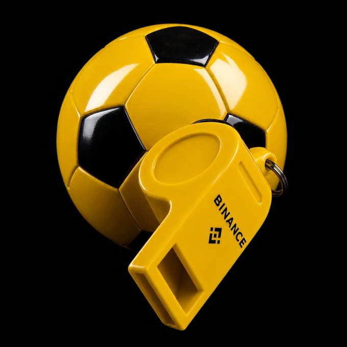 A 3D render of a yellow and black soccer ball with a yellow whistle attached, bearing the text "BINANCE" on the whistle.