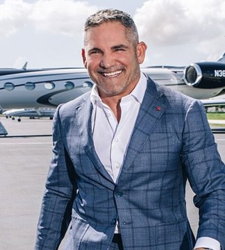 A man in a blue plaid suit jacket and white shirt smiling while standing outdoors with a private jet (tail number N36) visible behind him