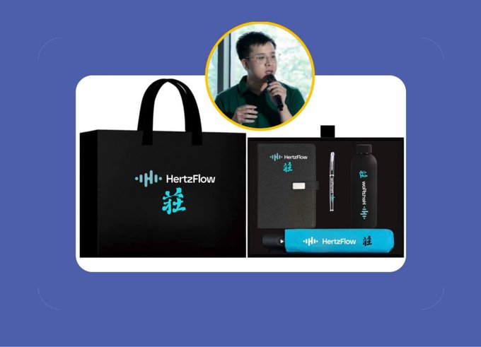 A promotional image for "HertzFlow" featuring a black gift bag and branded merchandise (notebook, pen, water bottle, pen case), along with a small circular photo of a man speaking into a microphone.