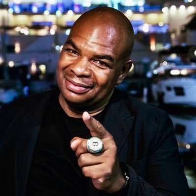 A smiling bald man in a dark suit points directly at the camera while wearing a prominent championship ring, likely at a sporting venue based on the blurred arena background. The image appears to accompany a crypto promotional message addressed to "Davinci Jeremie," suggesting the ring-wearing figure may be intended to represent the recipient of the pitch about the $wkc (WikiCat) token.