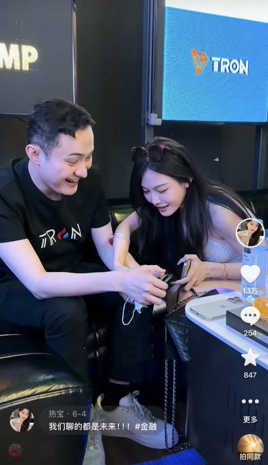 A short video screenshot showing Justin Sun (founder of TRON) laughing with a young woman at a TRON-branded event, with Chinese text reading '热宝·6-4 我们聊的都是未来！！！#金融' and showing 1.1万 likes and 847 favorites.