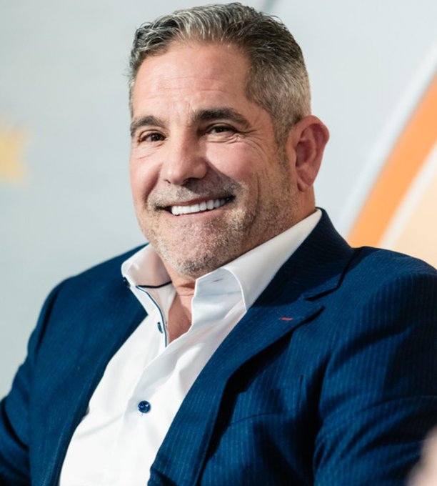 A smiling older man with gray hair and a stubble beard wears a blue blazer over a white shirt, posing for a portrait.