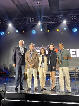 The image features a group of five people standing together on stage, posing for a photo. They are all dressed professionally, with one person wearing a suit and tie, another in a black dress, and three others in suits or business attire. The backdrop is a large screen displaying the words "Philippines Country Lead at @XDC_Philippines", indicating that this event may be related to Philippine blockchain initiatives or discussions on the adoption of blockchain technology within the country's economy.
