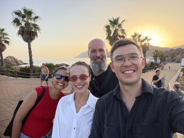 A group of four friends poses for a selfie at sunset near a beach with palm trees, with the ocean and distant hills visible in the background, capturing the joyful reunion mentioned in the post.