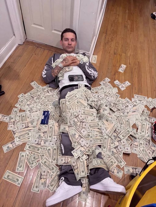A person lies on a wooden floor covered in scattered US dollar bills (mostly $20 and $50 denominations), with an image of currency displayed on their shirt. The post humorously celebrates a small 10% gain on a meme cryptocurrency, joking that they can now retire despite the modest profit.