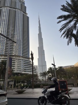 Photo of Burj Khalifa in Dubai with a person on a motorcycle in the foreground and palm trees visible.