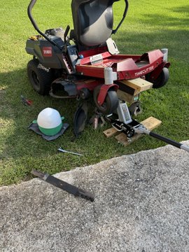A red zero-turn lawn mower, appearing to be a Toro or similar brand, is being repaired or modified in a grassy yard, with tools like a wrench and screwdriver scattered nearby along with a detached metal part. The image aligns with the post about being "in the midst of something special" with the $cupsey ticker, suggesting the mower is undergoing a significant upgrade or restoration project.