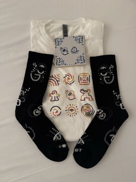 The image features two pairs of socks - one black and white, and another with colorful designs. The socks are placed next to a white t-shirt that has a drawing of a face on it. The text "GLiF Morning If you'r in Lisboa, stop by the shipping container gallery for Day 2. Get a pair of GLiFSocks!" is written above the image, suggesting that these items might be available at a location where GLiFSocks are sold or displayed.