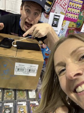 An excited man and woman pose with an Amazon package containing sunglasses in what appears to be a collectibles or trading card shop.
