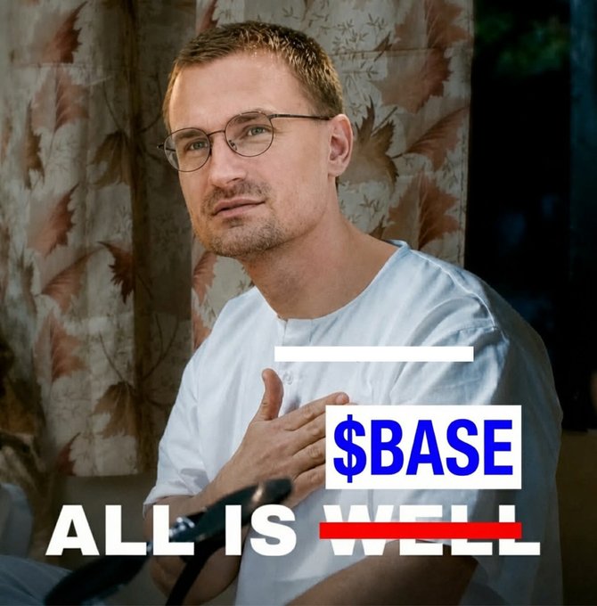 The image features a man wearing glasses, sitting down with his hand placed over his heart. He has short hair and is dressed in a white shirt. In front of him, there's an advertisement for $BASE that reads "All is well". The main focus of the image is on the man and the text displayed behind him.