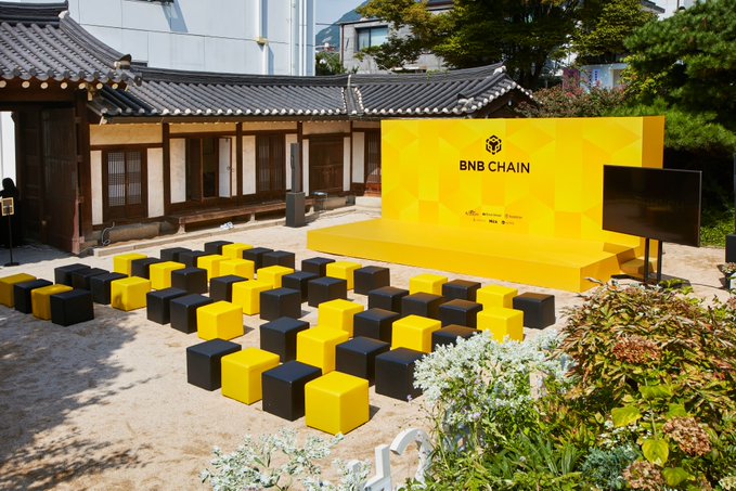 The image shows an outdoor event setup at a traditional Korean hanok venue, featuring black and yellow cube seats arranged in rows facing a bright yellow stage branded with "BNB CHAIN" alongside partner logos like Nexon and SKALA. The setup corresponds to the "#BNBSeoul" event, providing a branded presentation space for the BNB Chain gathering on October 2.