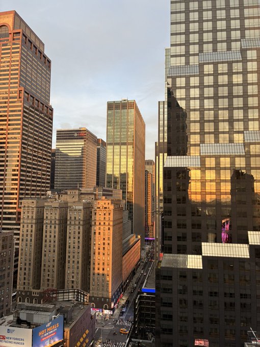 A stunning golden-hour view of Manhattan's Midtown skyline, with sun-warmed skyscrapers lining 8th Avenue and a yellow taxi visible below, ready to set the tone for a productive day in NYC.