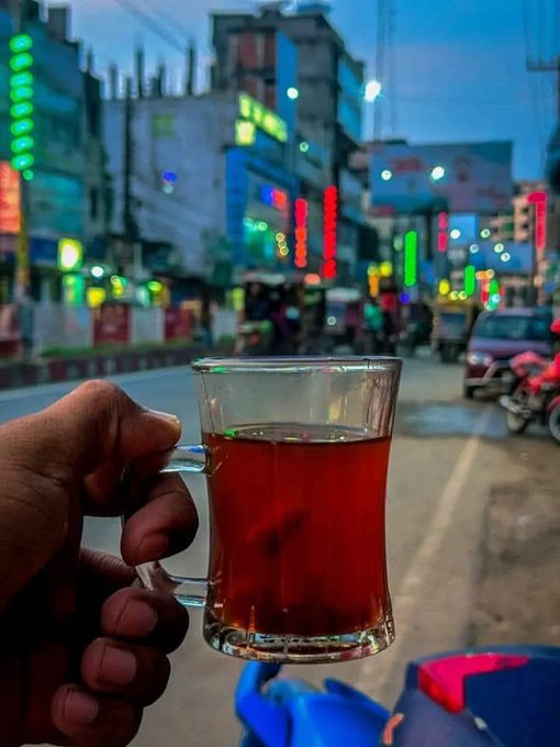 A hand holds a glass of tea against a blurred evening street scene illuminated by colorful neon signs, while the post sends a heartfelt goodnight message of gratitude to Web3 communities and fellow builders like Nucleus, CNPY, and Sleepagotchi—capturing the calm, reflective close of a productive day.