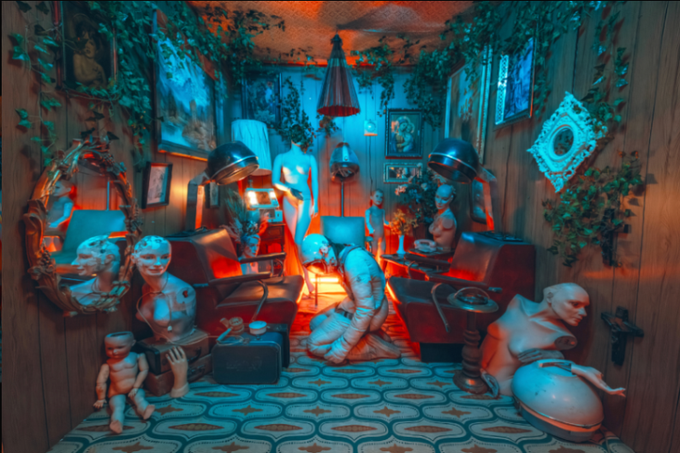 A surreal, atmospheric salon scene bathed in dramatic red and blue lighting, filled with overturned mannequin parts, vintage chairs, mirrors, framed portraits, and ivy creeping across wood-paneled walls, all arranged above an ornate patterned tile floor—mirroring the unsettling, theatrical aesthetic of the creator's self-portrait NFT titled "My Favorite Salon," available on OpenSea via the Ethereum blockchain.