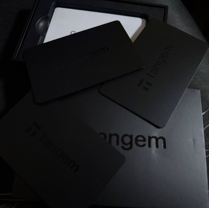 Three black Tangem hardware wallet cards are scattered on top of their packaging, with the brand name 'tangem' visible on each card and the box.