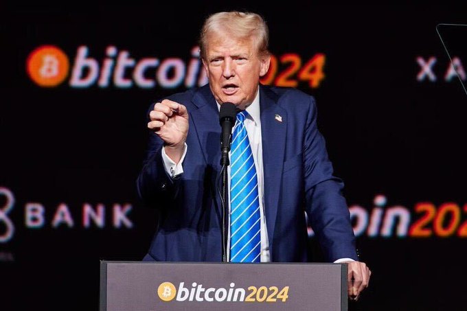 Donald Trump speaks at an event with "bitcoin2024" displayed on screens behind him and on a podium, aligning with his reported positive statements about Bitcoin and its impact on the dollar.