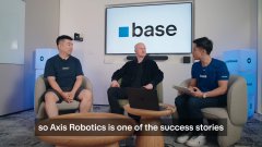 Three men sitting on a stage at a Base event, with subtitles reading 'so Axis Robotics is one of the success stories'.